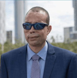 recent image of qusay hussein in a business suit with eye glasses. Austin skyline in the background